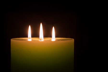 Candle with three flames on black background with copy spaceの写真素材