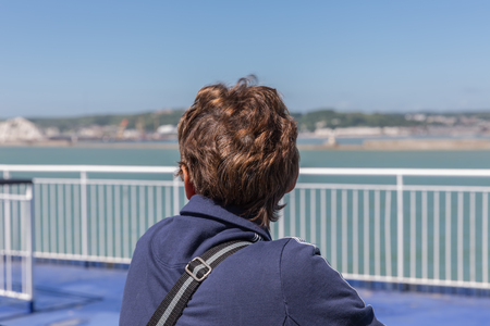 Woman at ferry leaving Dover looking backwards to the English coastの写真素材