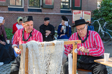 Urk, The Netherlands - September 02, 2017: Two men in traditional clothing mending fishing nets at a local fair with old costumes in Dutch village Urk, At the background other traditional people.のeditorial素材