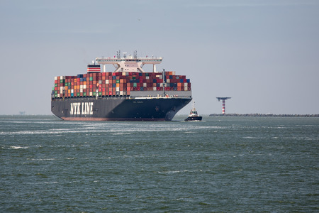 Rotterdam, The Netherlands - June 5 2018: Big cargo ship with containers sailing with tugboat into...