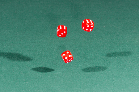 Three red dices falling on a isolated green table