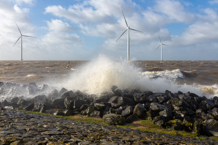 Dutch sea with off shore wind turbines and breaking waves at the shoreの写真素材