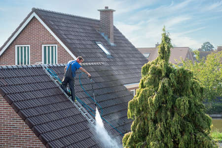 Urk, The netherlands - September 15, 2020: Cleaner with pressure washer at roof of house cleaning the roof tiles, removing moss and weedのeditorial素材
