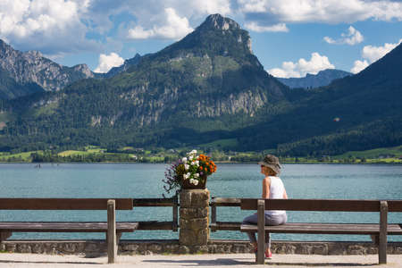 Sankt Wolfgang, Austria - Juli 19, 2017: Unknown woman with sunbonnet sitting at wooden bench in Sankt Wolfgang near Austrian Wolfgangseeのeditorial素材
