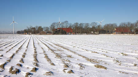 Dutch farmland covered by white snow with farmhouse and wind turbineの写真素材