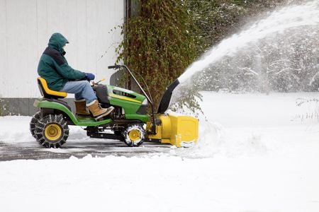 Side view of middle-aged man on riding snow blower, clearing snow out of residential drivewayのeditorial素材