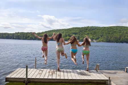 Four teenage girls jumping off a dock into Little Squam Lake--backの写真素材