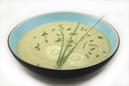 Cold avocado and cucumber soup in a turquoise bowl with cucumbers and chives, isolated on whiteの写真素材