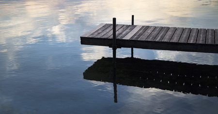 Dock on a lake with clouds reflected in waterの写真素材