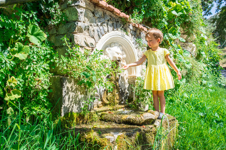 Little girl in yellow dress washes at source.のeditorial素材