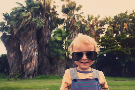Funny little boy in sunglasses next to palm trees in the tropical countryの写真素材