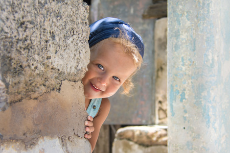 Pretty boy with white curly hair peeping out ancient wall.の写真素材