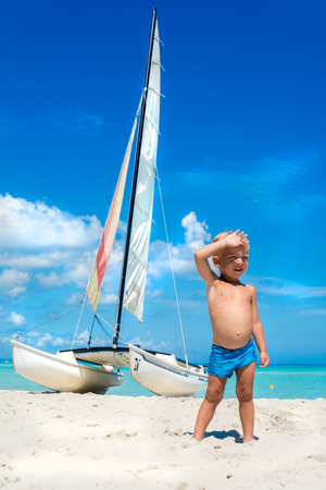 Young boy standing on ocean coast with the yacht on the background. Vacation with kids.の写真素材