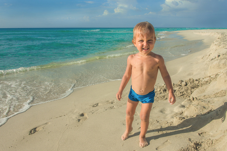 Little boy standing on the white sand beach and squinting from the sun.の写真素材