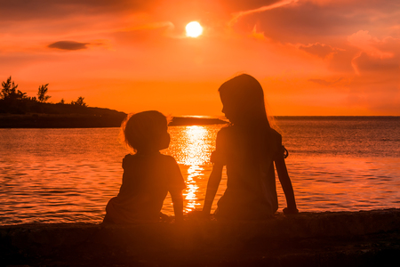 Little sister and brother silhouettes at the sunset.の写真素材