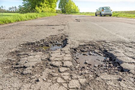Road in terrible condition. Photo of a road with potholes. Car is on background.の写真素材