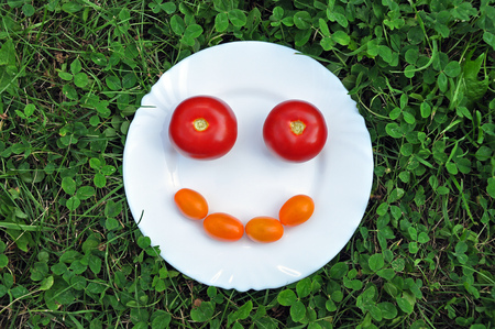Smiling smiley made of orange and red fresh tomatoes on a white plate.の写真素材
