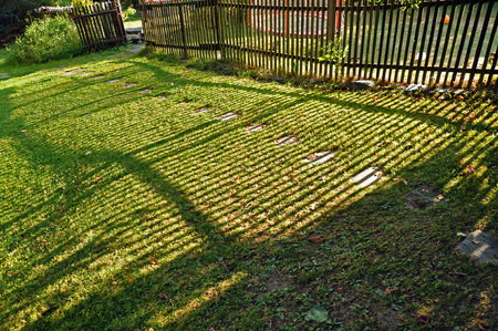 Old wooden fence makes shadows on a green lawn.の写真素材
