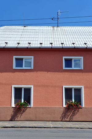 The front of the house with four windows with flowers and a tin roof with an antenna.の写真素材