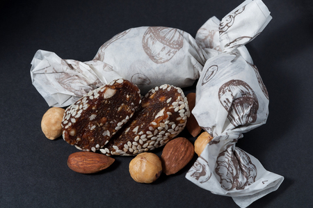 one cut candy with sesame and two wrapped handmade candies are lying near the nuts on a black background. Close-up viewの写真素材