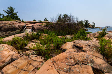 A wooden footbridge over rugged granite rocks on a trail along the coast of Georgian Bay. Killarney Provincial Park, Ontario, Canadaの写真素材