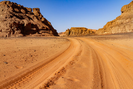 Empty sandy dirt road with tire tracks in Tassili National Park. Tadrart mountains, Acacus range. Tassili N'Ajjer National Park. Algeria, Africaの写真素材