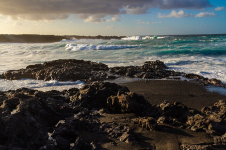 Black volcanic rocks on the Atlantic coast at sunset. Playa de las Malvas, Lanzarote, Canary...