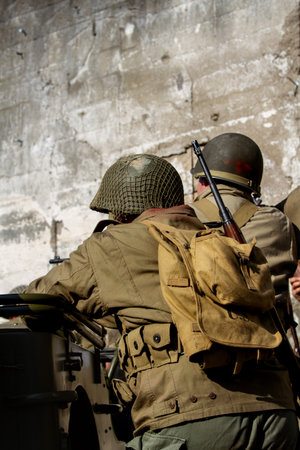 Historical reconstruction. An American infantry soldiers from the World War II prepare to attack hidden behind a milirary vehicle. View from the backの写真素材