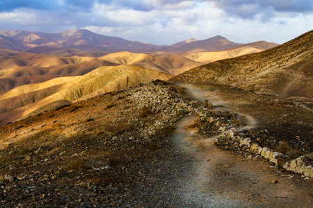 Hiking trail to Melindraga mountain. A narrow twisting path passing through rough deserticolous landscape volcaic moutains. Fuerteventura, Canary islands, Spain,の写真素材