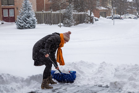 A young woman shovels snow from a her driveway during  snowstorm. January 2026, Oakville, Ontario, Canadaの写真素材