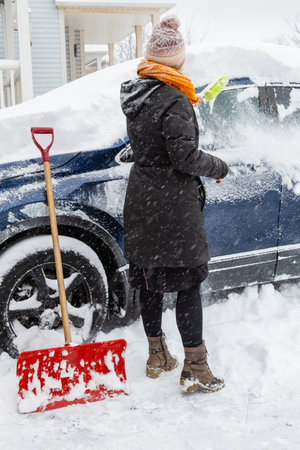 A young woman clears snow from her car during a snowstorm. January 2026, Oakville, Ontario, Canada.