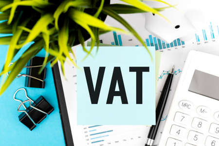 Text VAT - Value-Added Tax on blue sticker, calculator, pen, piggy, graphs, plant. Business flat lay.の写真素材