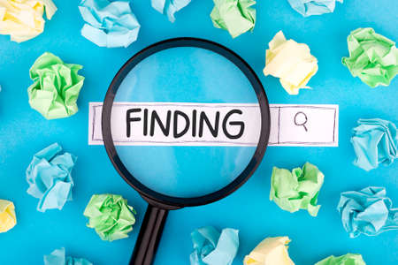 Concept of searching. Text FINDING with magnifier and pieces of paper on blue background.の写真素材