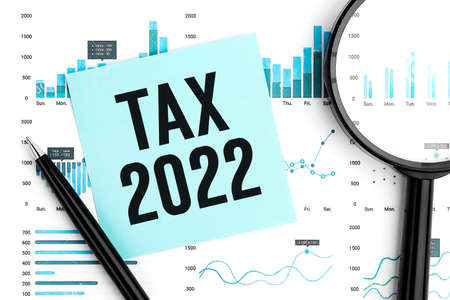 Text TAX 2022 on sticker. Pen and calculator on clipboard with charts, documents and graphs. Business concept. Flat lay. Tax deduction planning concept.の写真素材