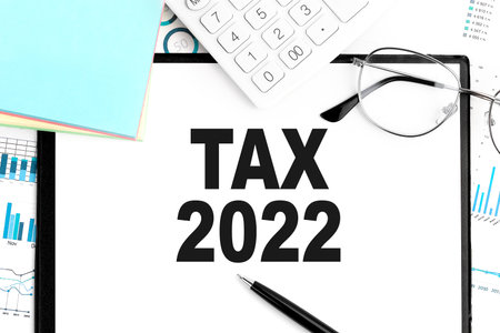 Text TAX 2022 on clipboard, pen, glasses, calculator, sticker, graph. Business concept. Flat lay.の写真素材