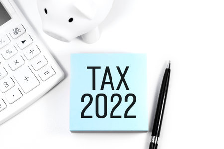 Text TAX 2022 on sticker, piggy, calculator. Business concept. Flat lay.の写真素材