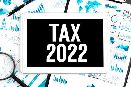 Text TAX 2022 on tablet. Clipboard, pen, magnifier, chart, document and graph background. Business concept. Flat lay.の写真素材