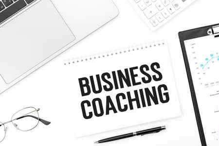 Text BUSINESS COACHING on notebook, laptop, calculator, pen, glasses.の写真素材