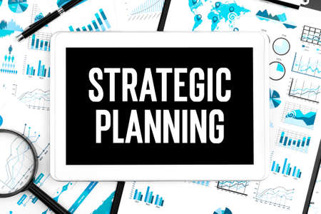 Text STRATEGIC PLANNING on tablet, magnifier, graphs. Business concept. Flat lay.の写真素材