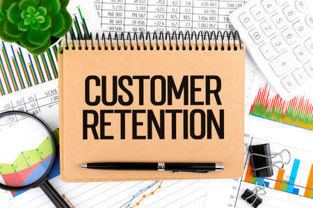 Text CUSTOMER RETENTION on notebook, calculator, magnifier, charts. Business concept, flat lay.の写真素材