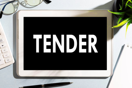 Word TENDER on tablet, calculator, glasses, notebook, pen on office desk. Business concept.の写真素材