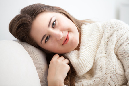 Brunette woman smiling and sitting on sofa in living roomの写真素材