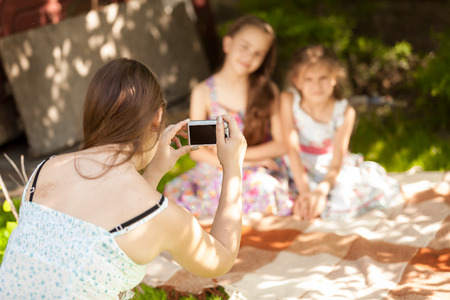 Young beautiful mother making photo of daughters on picnicの写真素材