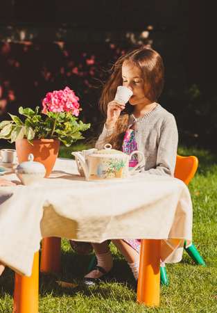 Beautiful cute girl drinking tea at toy table at yardの写真素材