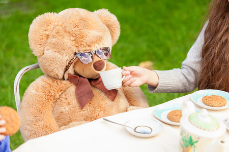 Cute girl giving tea to teddy bear at yardの写真素材