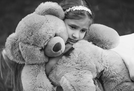 Black and white portrait of small crying girl hugging teddy bearの写真素材