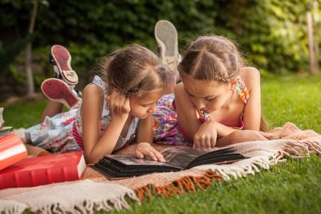 Cute girls lying on grass at park and looking at old family photosの写真素材