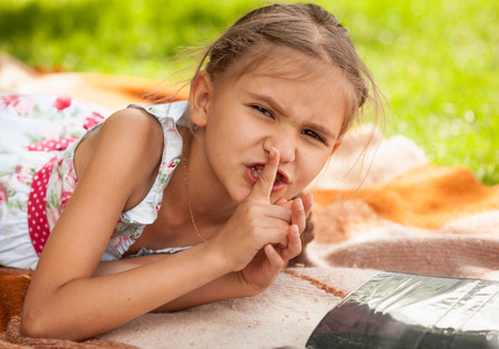 Portrait of little girl lying at park and holding finger at lipsの写真素材