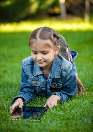 Closeup shot of little girl lying on grass with tabletの写真素材