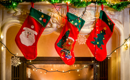 Three red christmas stockings hanging on decorated fireplaceの写真素材